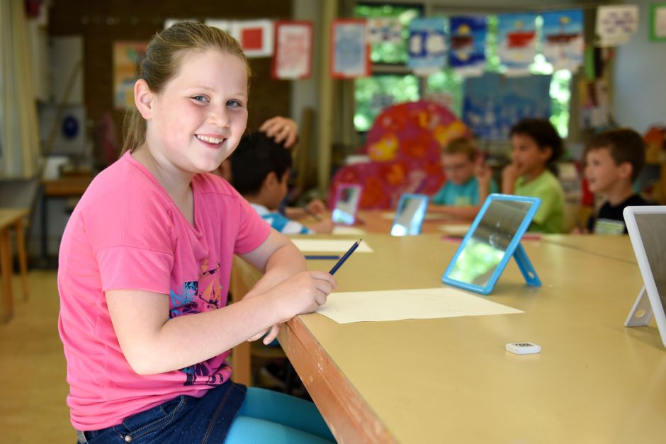 Niña escribiendo un cuento creativo con apoyo de una tableta y un cuaderno